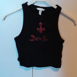 Svart crop-top - En svart crop-top med ett kors och text. Trycket är i akrylfärg men har blivit lite slitet.
