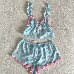 Tezenis pyjamas set med blommor - Otroligt vackert gingham-rutigt pyjamasset med blommor från Tezenis. Storlek L i shortsen och S i toppen. Nytt med tags kvar, utan anmärkningar.