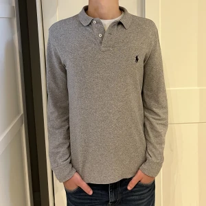 Långärmad Ralph Lauren piké  - Långärmad Ralph Lauren piké i färgen grå. Inga defekter på tröjan. Size M (slim fit) modellen är 177cm. Hör av dig vid funderingar!