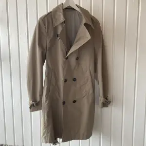 Fin trenchcoat från Tiger of Sweden, made in Italy 🇮🇹 Inköpt på NK för ca 4000kr.  Vadderade axlar och vattenavstötande nylon. Skärp i midjan, går att både styla och knäppa denna på flera olika sätt. Fint skick! Strlk 48. Hör av dig vid frågor. 