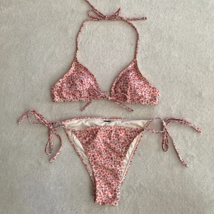 Blommig bikini - Trekantsbikini i rosa blommigt mönster med knytdetaljer och uttagbara inlägg, originellt från NA-KD! Aldrig använd utan endast testad av mig, tvättad 👙