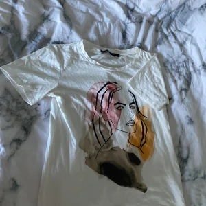 T-shirt med tryck  - Säljer denna vita t-shirt som har ett tryck på framsidan vilket efterliknar en kvinna. Använd vid ett tillfälle. 