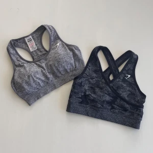 Gymshark Bh-ar  - Två sport bh-ar från gymshark. Grå är vital seamless och Mörkgrå/svart är camo. Priset är för båda, skriv om du bara är intresserad av en! 🥰 