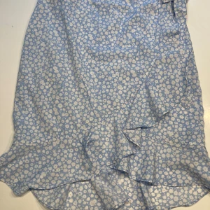 Omlottkjol med volanger  - Mycket fin omlottkjol med volanger  Ljusblå med vita blommor.  Knytes i midja 