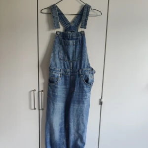 Hängselbyxor - Blå hängselbyxor/dungarees i jeans från H&M. Storlek 34. Justerbara band. Fint skick, säljes då de inte passar mig