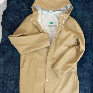 STUTTERHEIM regnjacka  - Snygg regnjacka från STUTTERHEIM perfekt till blöta sommardagar! Senapsfärgad. Jackan har några få fläckar, säljer därför billigt. Hel och bra annars! 