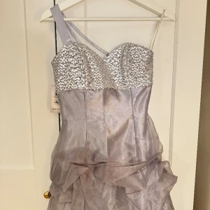 Superfin klänning - Vacker, unik klänning med prislappen kvar. Storlek XS/S. Det är en kort klänning i silver, paljetter och volang. Märket är JessicaMcClintock.  Hör av er vid frågor!