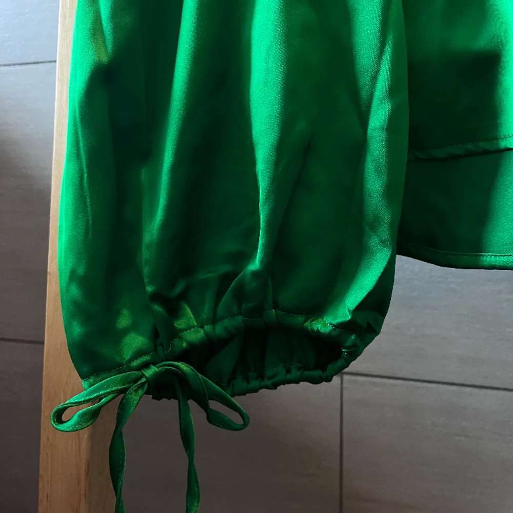 Festlig satin-blus i härlig grön färg och rosett detaljer vid ärmarna. Den är aldrig använd och har lapparna kvar. Storlek 36 💚. Blusar.