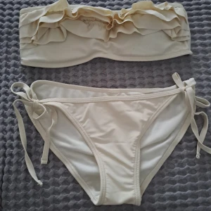 Bikini sett - Off white bikini sett från bikbok Off shoulder det går att sätta dit ett band om man vill det går även att ta ut inläggen,överdelen är använd fåtal gånger. Liten defekt på spännet (se sista bild) SKICKAR EJ BILDER MED BIKININ PÅ!!!!
