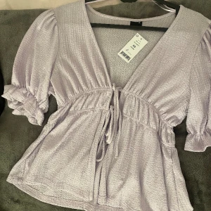 Ljuslila sommar blus - aldrig använd, prislapp är kvar. jätte fin blus som går att ha ett linne under eller bara knyta snörena. passar perfekt t sommaren. har tyvärr inga bilder med den lila på endast i den vita modellen! kom privat för bättre bilder. köpte för 250kr<3