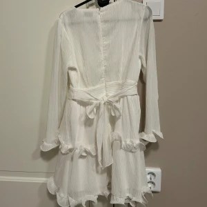 Vit klänning med volanger - Super fin vit klänning med rosett i ryggen och volanger! Perfekt till student, konfirmation eller annat firande