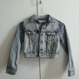 Croppad jeansjacka - Från "Detroit by Lindex" Storlek 140 barn Liten missfärgning på ena ärmen, se bild 3, annars gott skick 98% bomull 2% elastan Skicka pm för mer info/samtal