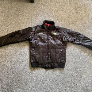 Puma racing jacka - Svart Puma Ferrari jacka i cool racing stil med många detaljer. Lite slitage vid kajen annars i mycket bra skick!