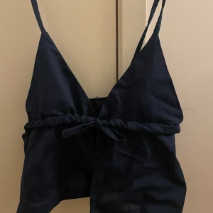 Marinblå sommartopp - En jättesöt mörkblå sommartopp, som nog passar folk i storlek XS eller mindre byst. Man knyter toppen framtill med rosetten. Jättesöt men tyvärr för liten för mig.