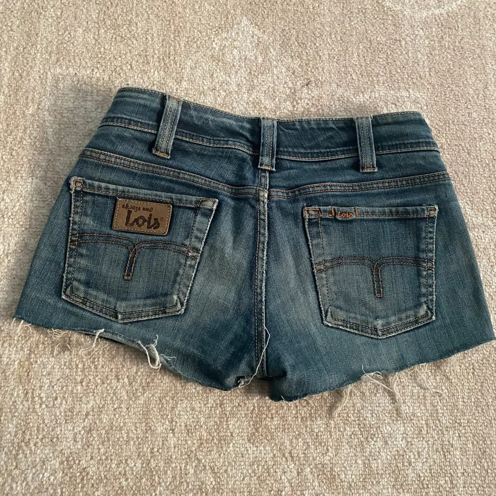 Säljer ett par mörkblå jeansshorts från Lois i storlek 34. De är lågmidjade och har en snygg, sliten look med fransiga kanter. Perfekta för sommaren! Shortsen har fem fickor och knappar samt dragkedja framtill. De är i bra skick och redo för en ny ägare.. Shorts.