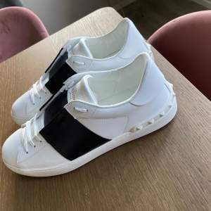 Säljer ett par snygga Valentino Garavani sneakers i vitt och svart. Skorna är i skick 10/10 endast använda 1 gång utomhus och kommer med originalförpackning och extra skosnören. De har en cool design med svarta detaljer och nitar på sidorna. Perfekta för både vardag och fest!