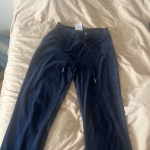 Mörkblå mjukisbyxor med matchande hoodie - Säljer ett set med mörkblå velour/mjukisbyxor och en matchande hoodie/kofta. Byxorna har en dragsko i midjan för justerbar passform och hoodien har en dragkedja framtill. Perfekt för mysiga dagar hemma eller en avslappnad dag ute. Setet är i bra skick och superbekvämt!