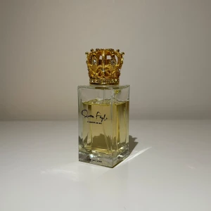 Lyxig parfym med guldkrona - Säljer en superlyxig parfym med en elegant guldfärgad krona som lock. Flaskan är fyrkantig och genomskinlig, vilket gör att den gyllene vätskan inuti syns tydligt. Perfekt för den som vill känna sig som en drottning varje dag! Flaskan är både stilren och extravagant, vilket gör den till en perfekt present eller en lyxig detalj på sminkbordet. Köp nu och dofta fantastiskt! 💛