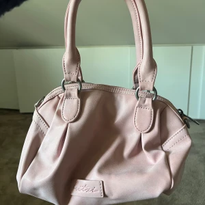 Rosa väska - Säljer nu min rosa väska köpt från ett märke på zalando ( kommer ej ihåg märket, kan leta upp om någon undrar ). Man kan bära den i handen eller med bandet som medkommer, kommer även med en liten gullig tofs man kan sätta på väskan ! 🩷🌸köpt för 600kr
