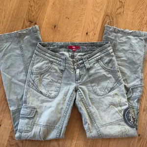 Low waist cargo jeans - As snygga militärgröna cargo jeans i low waist+bootcut med broderi och stenar på låren. I bra skick förutom lite slitningar bak vid hälarna och knapparna på bakfickorna saknas (se bild). Midjemått 40 cm rakt över, innerbenslängd 82 cm. 💚🩶
