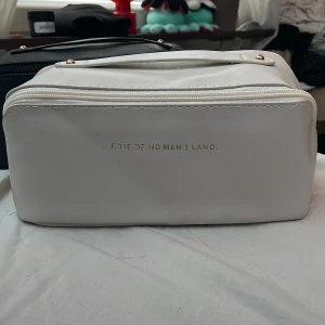 Vit necessär från Rose of No Man's Land - Säljer en snygg och praktisk vit necessär från Rose of No Man's Land. Den är tillverkad i syntetmaterial och har en dragkedja upptill. Insidan är rymlig med flera fack för att organisera dina saker. Perfekt för resor eller att ha hemma för att hålla ordning på dina skönhetsprodukter.