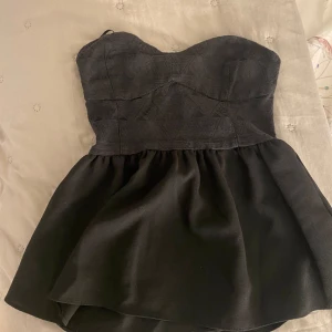 Svart axelbandslös top - Säljer en elegant svart axelbandslös top. Den har en tight passform upptill och utsvängd nedtill. toppen är i nyskick och redo att användas.