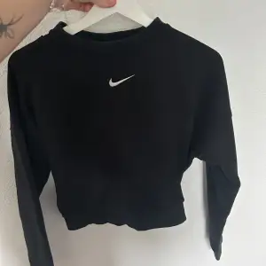 Säljer en svart croppad tröja från Nike. Den har en liten vit Nike-logga på framsidan och en öppen rygg. Tröjan är långärmad och perfekt för både träning och vardagsbruk. Den är i nyskick och väldigt bekväm att ha på sig. Passar perfekt till höst och vår!