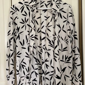 Vit blus med svart blommönster från MNG - En elegant vit blus från Mango med ett svart blommönster. Blusen har långa ärmar och en klassisk krage. 