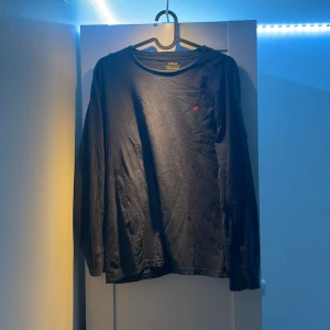 Marin blå långärmad tröja från Polo Ralph Lauren - Säljer en  långärmad tröja från Polo Ralph Lauren. Tröjan är i storlek L och har en liten röd broderad logga på bröstet. Perfekt för höst och vinter, den är både stilren och bekväm.passar  till både vardag och fest. Hör av dig om du är intressera