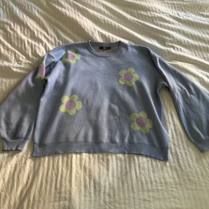 Ljusblå stickad tröja från Daisy Street - En ljusblå stickad tröja från Daisy Street med gula och rosa blommor på. Jag fick den som en gåva för 3 år sedan. Storlek XXL men passar mer som en XL eller kanske L