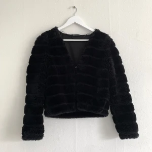Svart faux fur-jacka - Hake och hyska är ditsydd för att kunna ”stänga” den lite.