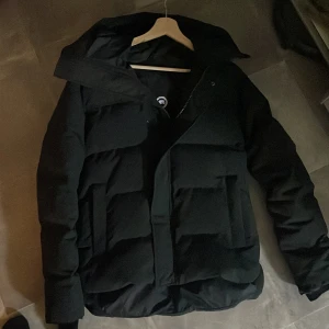 Canada Goose Jacka - Äkta -  Säljer en helt äkta och som ny Canada Goose vinterjacka. Jackan är i perfekt skick (10/10) och har knappt använts. Detaljer	Justerbar huva Flera fickor med dragkedja och knappstängning Ikonisk Canada Goose-logga på ärmen 	Hög krage för extra skydd 