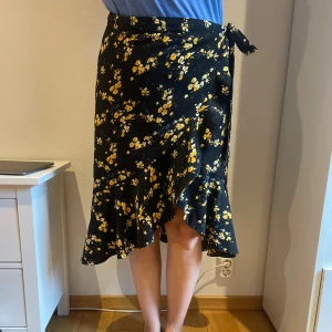 Blommig kjol - Somrig kjol från Cubus.  Fint skick. Justerbar knapp att knäppa extra med utöver knytet.  Passar 40-46. (Finns en extra knapp med).