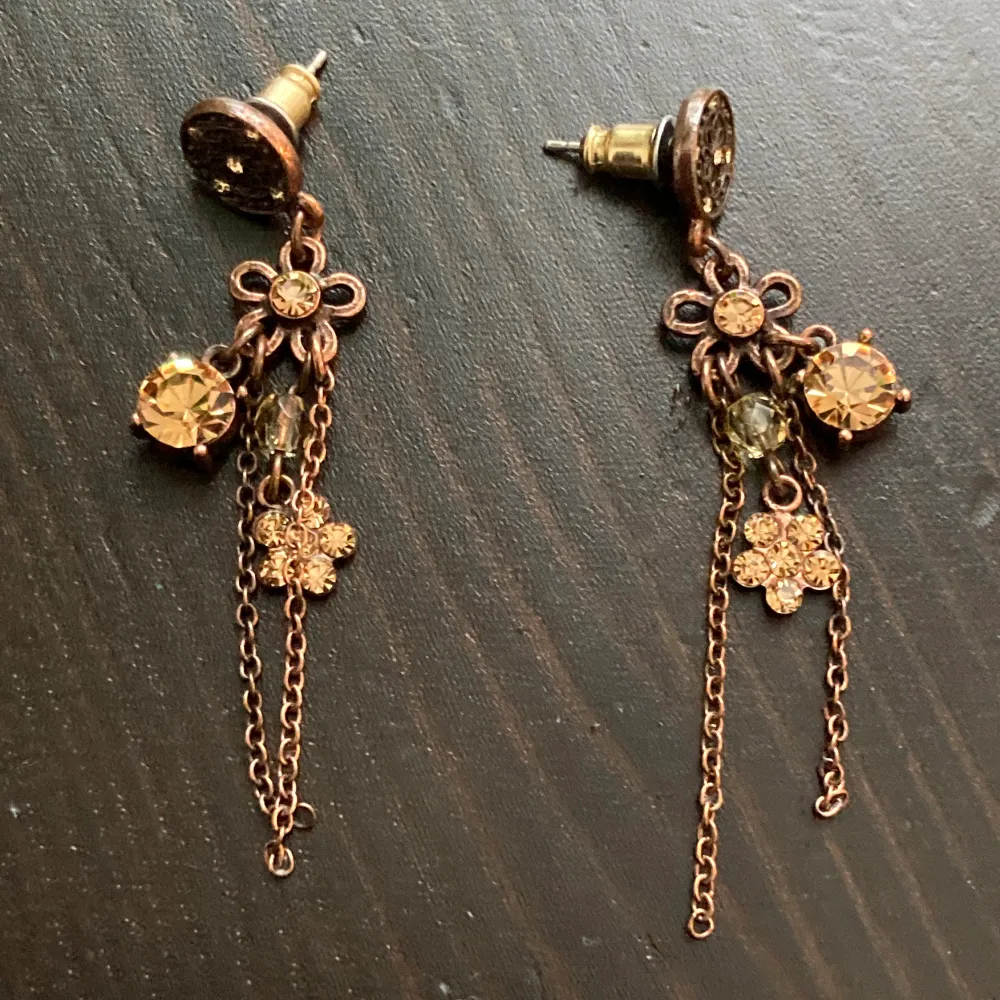 Bronsfärgade örhängen med berlocker och ljus orange strass. Längd: 5 cm.. Accessoarer.