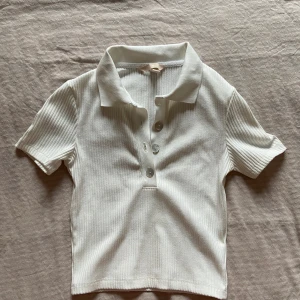 Ribbad pikétröja - Vit ribbad piké från H&M. Storlek S. En knapp saknas högst upp men extraknappen finns kvar på lappen inuti tröjan. 