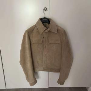 Säljer en oanvänd beige mockajacka från Tiger of Sweden.  Pris lappen sitter fortfarande kvar.  Nypris: 8999 kr  Storlek: 46  