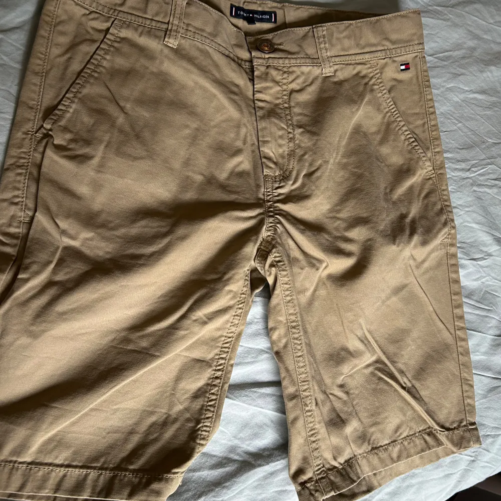 Beiga chinos shorts från Tommy Hilfiger.  Passar bra till åldern 14-15, stl 164. Shorts.