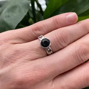 Aldrig använd. Ringen är i rostfritt stål med svart kristall, justerbar, ca 17-19mm. Nickelfritt, levereras i smyckespåse. Fin present. Djur- och rökfritt hem. Nypris 399kr
