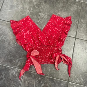 Rödprickig topp - Aldrig använd, super söt med väldigt många detaljer, v-ringning både fram och bak, resår för att få midjan med markerad och även små söta rosetter (man kan själv knyta om rosetterna) , aningens croppad