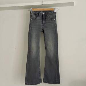 Grå bootcut jeans i strlk 134. Superfina och som nya! Tvättade en gång men inte använda, då de blev för små för fort.  Stretchiga bootcut-jeans med medelhög midja och fem fickor. Trendiga och bekväma jeans med reglerbar resår på insidan av midjan. 