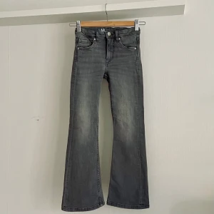 Bootcut grå jeans - Grå bootcut jeans i strlk 134. Superfina och som nya! Tvättade en gång men inte använda, då de blev för små för fort.  Stretchiga bootcut-jeans med medelhög midja och fem fickor. Trendiga och bekväma jeans med reglerbar resår på insidan av midjan. 