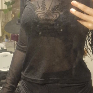 Genomskinlig y2k topp - Genomskinlig y2k topp med mönster över kistan. See through y2k black top with a heart pattern on the front