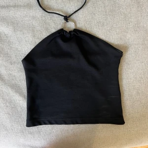 Partytopp - Svart linne, påminner om en halterneck linne. Knute i nacken och ringen sitter på framsidan vid bröstkorgen. Öppen i ryggen. Stretchig. Passar 34-38. 