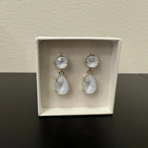 Mini Drop örhängen från Caroline Svedbom  - Örhängen i nyskick från Caroline Svedbom. Örhängena består av två runda och två droppformade gnistrande kristaller av högsta kvalitet. Stiftet som sitter i örat är tillverkat av 925 silver och förgyllt.