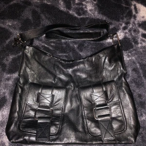 Svart axelväska i skinn - En svart axelväska i skinn med två framfickor med spännen och en dragkedjeficka på baksidan. Väskan har en justerbar axelrem , men lite slitningar som man kan se på 3 bilden. Skriv om du vill ha fler bilder eller frågor <3