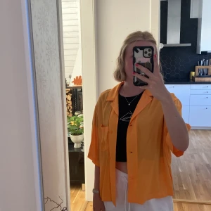 Orange skjorta  - Glansig orange skjorta som har använts två gånger från HM. Kan både användas som en skjorta, men också en färgglad ”kofta” för att få sätta härlig färg på sin outfit 