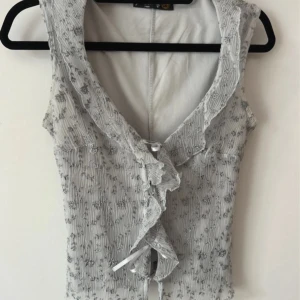 Söt grå top - Gråblå topp med blommönster, köpt på vinted men kommer ej till användning. Knyts med band längst fram. 