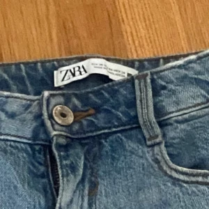 Blå jeans från Zara - Ett par blå jeans från Zara i storlek EUR 36 / US 04 / MEX 26. Jeansen har en klassisk femficksdesign och är tillverkade i Bangladesh. De har en knapp och dragkedja framtill samt en läderlapp med 'Zara Denim' på baksidan.
