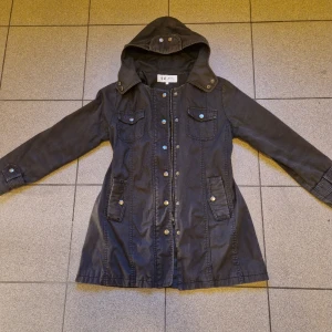 Svart jacka med knäppning - Dragkedja och knäppning. Fickor Fodrad vida armar Luva