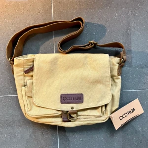 Ny Gootium canvasbag med fickor - Helt ny, oanvänd Gootium axelbandsväska med hållbart canvastyg, fickor till allt du behöver och gott om utrymme utan att den är stor. Nätt, väger ingenting och hänger snyggt på höften. Perfekt till en liten laptop, böcker, plånbok, allt! 